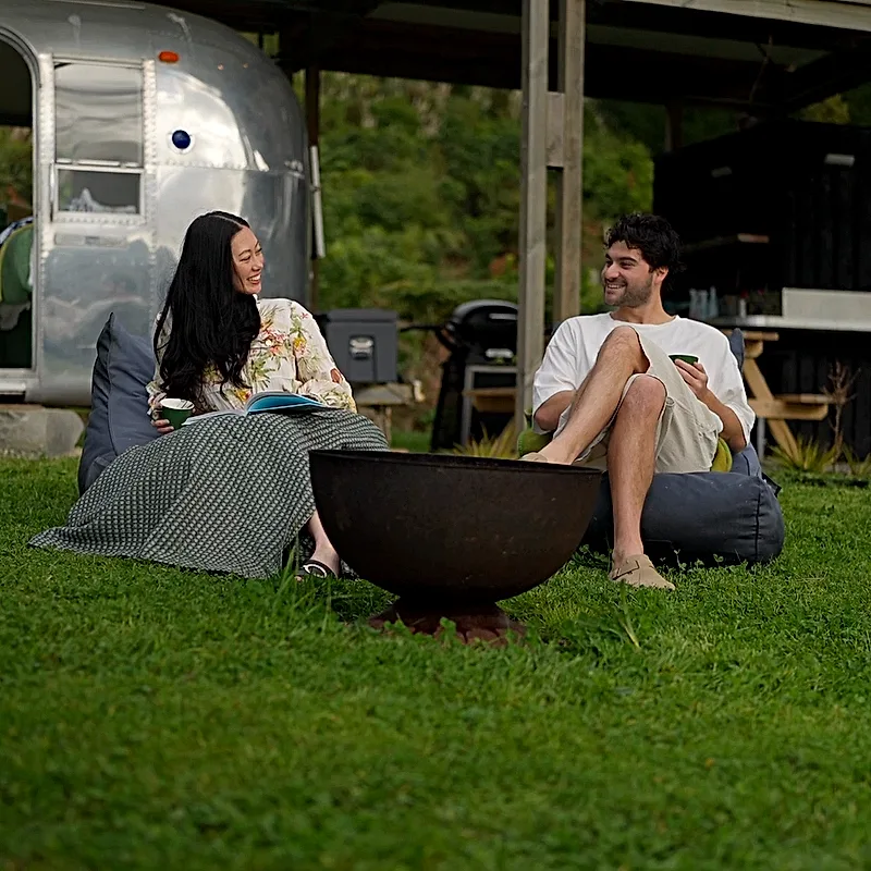 Two guests laughing over coffee by the fire pit outside the Airstream