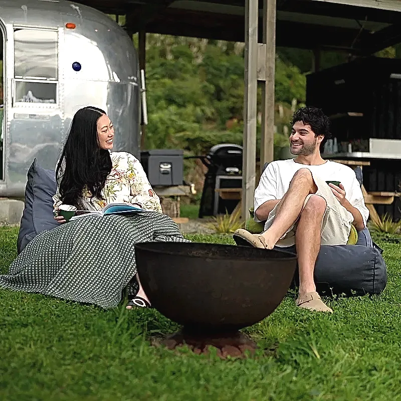 Two guests with coffee by the fire pit outside the Airstream