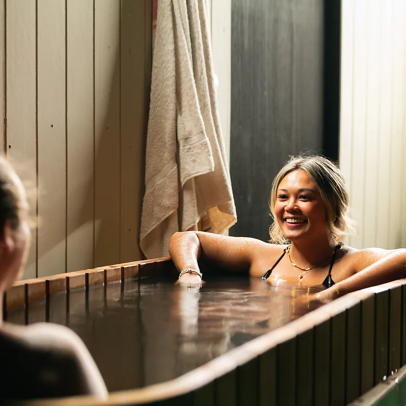 A guest smiling in the cedar hot tub, arms resting on the rim