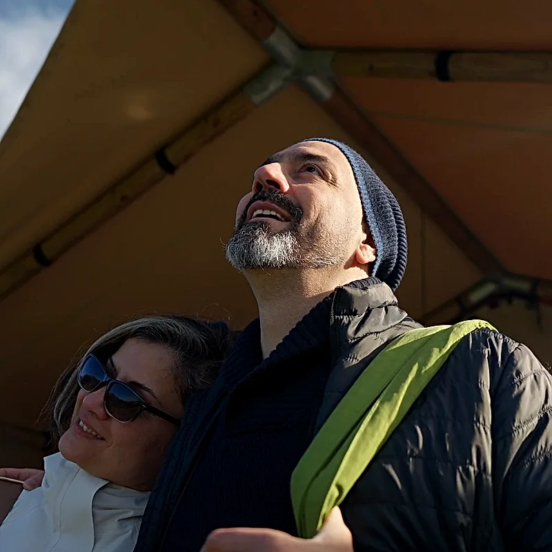 A couple arm in arm under the safari tent canopy, smiling up at the sky