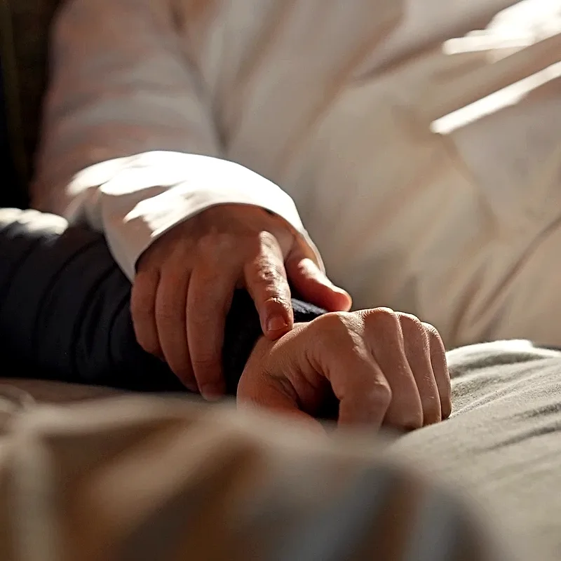 Two hands held together on the bed inside the safari tent, in warm afternoon light